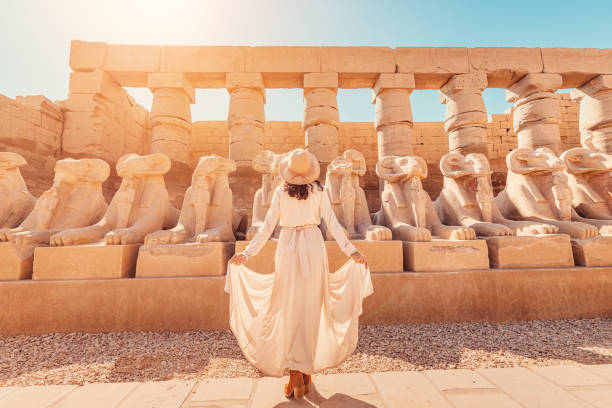 A happy tourist girl interested in Egyptology and archaeology and gets a travel experience at the Karnak Temple in Luxor among alley of sphinxes in Thebes